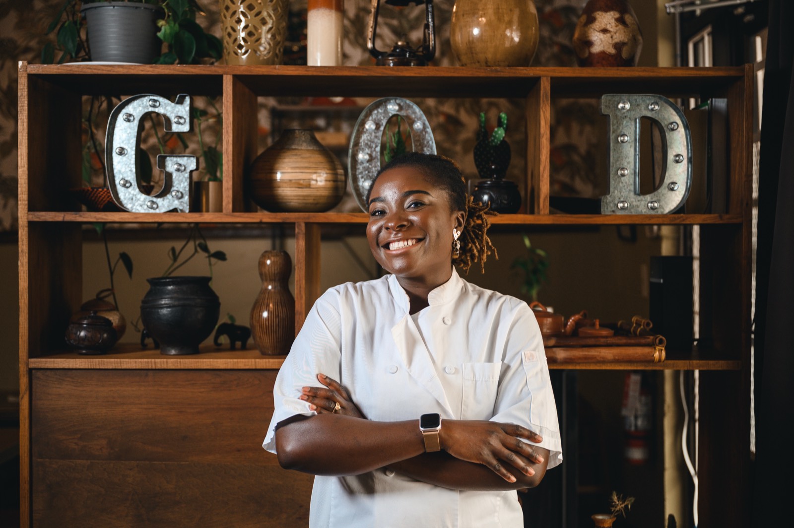 The chef-owner in front of a styled shelf spelling GOOD in metal letters.