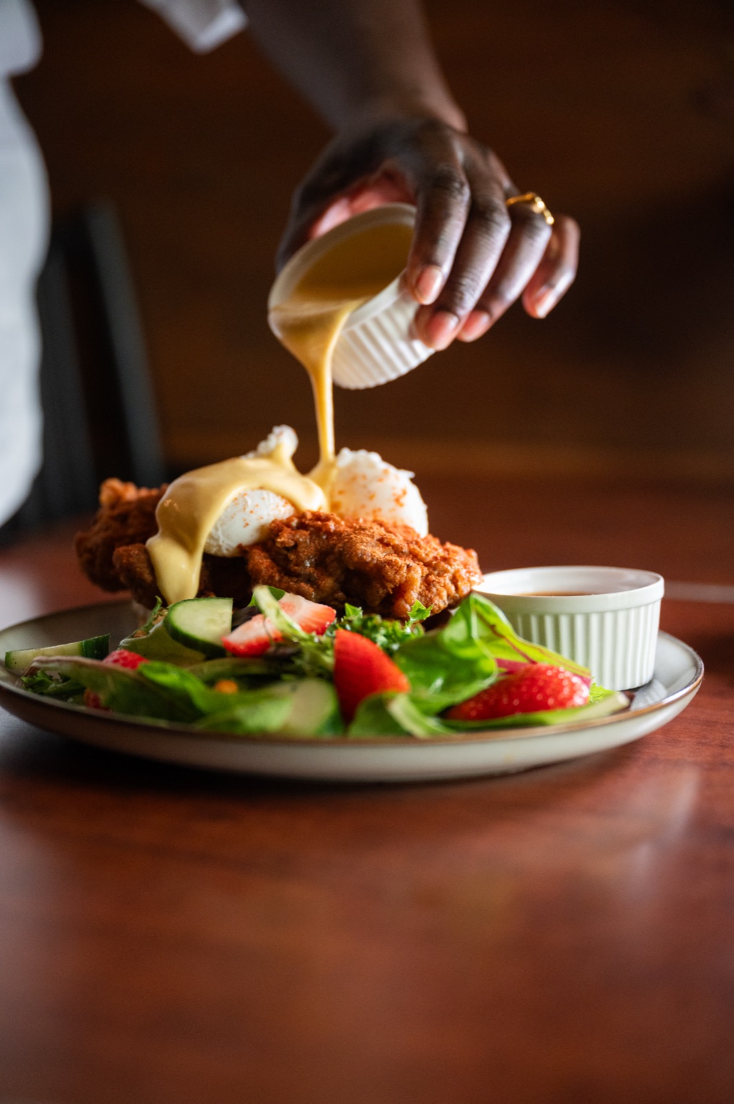 Hollandaise being poured over suya chicken and waffles.