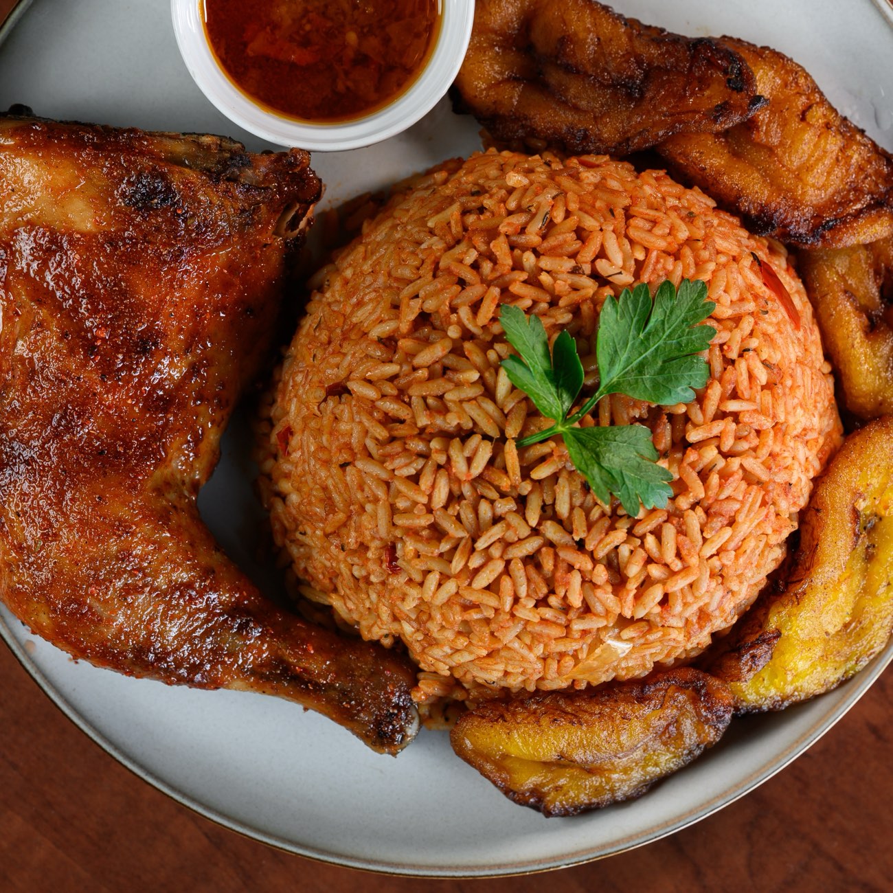 Overhead plate of jollof rice with grilled chicken, fried plantain and pepper sauce.